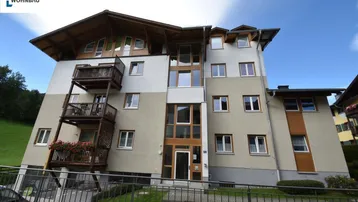 Mehrstöckiges Wohngebäude mit mehreren Balkonen und moderner Fassadengestaltung unter blauem Himmel.