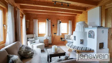 Helles Wohnzimmer mit Kachelofen, bequemen Sofas und Holzbalkendecke in alpiner Atmosphäre.