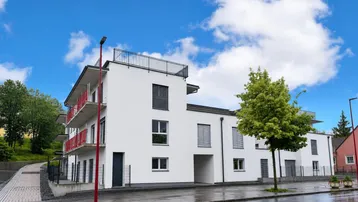 Modernes Mehrfamilienhaus mit weißer Fassade, Balkonen und Flachdach unter blauem Himmel.