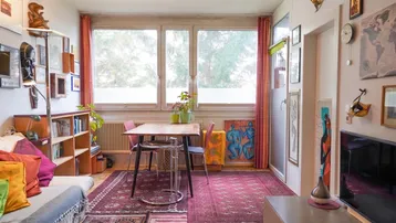 Gemütliches Wohnzimmer mit Essbereich, bunten Teppichen und Blick ins Grüne durch große Fenster.