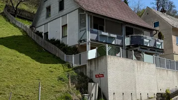 Haus an einem Hang mit mehreren Balkonen und einer steinernen Stützmauer.