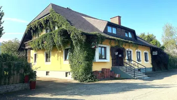 Traditionelles gelbes Gebäude mit üppigem Efeu bewachsen und einem Satteldach unter blauem Himmel.