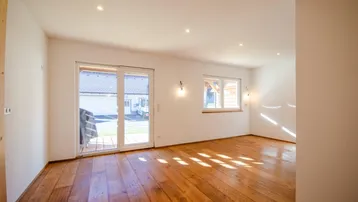 Helles, leeres Zimmer mit Holzboden, großen Fenstern und Zugang zur Terrasse.
