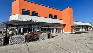 Modernes Geschäftsgebäude mit auffälliger orangefarbener Fassade und großem Parkplatzbereich davor.
