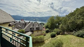 Panoramablick auf den See und die umliegende Landschaft mit Häusern und grünen Hügeln unter bewölktem Himmel.