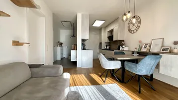 Heller offener Wohn-Essbereich mit Holzboden, modernem Sofa und integrierter Küche.