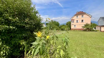 Weitläufiger Garten mit grüner Rasenfläche und dem historischen Gebäude im Hintergrund.