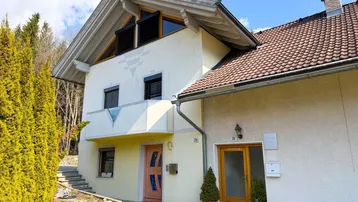 Vorderansicht eines charmanten Hauses mit hellgelber Fassade, Satteldach und kleinen Balkonen.