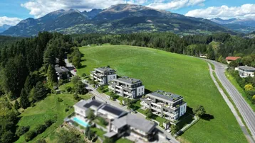 Luftaufnahme von modernen Neubauten in einer grünen Hügellandschaft mit Bergblick.