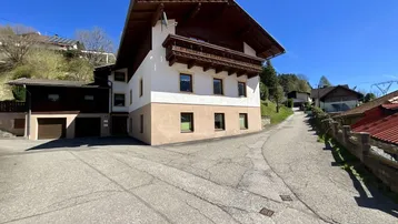Traditionelles Haus im alpinen Stil mit Holzbalkonen und weißer Fassade, umgeben von einer bergigen Landschaft.