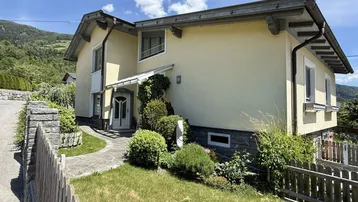 Vorderansicht eines Einfamilienhauses mit gelber Fassade und gepflegtem Vorgarten.