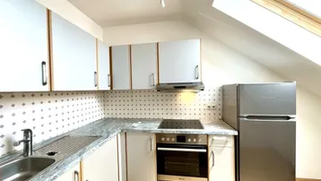 Funktionale Küche mit Dachschräge, Einbauschränken, Kühlschrank und Dachfenster.
