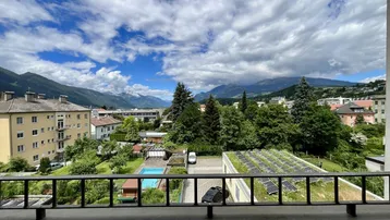 Blick vom Balkon auf die umliegende Berglandschaft, Gebäude und einen Poolbereich.