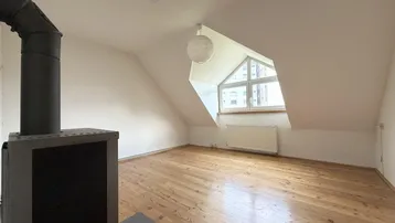 Dachgeschosszimmer mit Holzdielenboden, gemütlichem Kaminofen und charakteristischem Giebelfenster.