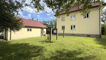 Großer Gartenbereich mit Rasenfläche und zwei Gebäuden unter blauem Himmel.