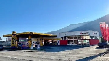 Außenansicht eines Gewerbegebäudes mit Tankstelle und WÜRTH-Filiale vor einer Bergkulisse.