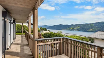 Langer Balkon mit Holzgeländer und weitem Blick über den See und die bewaldeten Hügel.