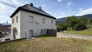 Hinterhof mit Rasenfläche, Steinmauer und Blick auf die umliegende Berglandschaft.