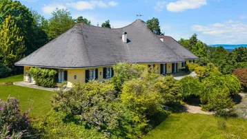 Luftaufnahme eines weitläufigen Anwesens mit gelber Fassade, großem Garten und Blick auf die Landschaft.