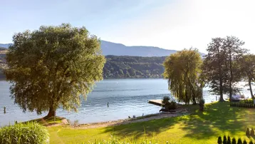 Malerischer Blick auf einen ruhigen See mit bewaldeten Hügeln und einem kleinen Steg.