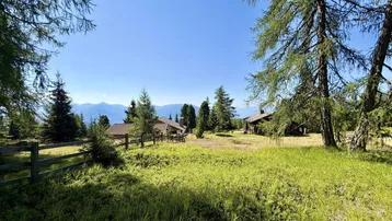 Weitläufige Wiesenlandschaft mit verstreuten Holzhäusern und Bergblick unter klarem Himmel.