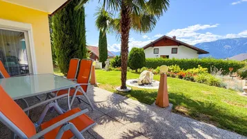 Sonnige Terrasse mit Gartenmöbeln, Palmen und Blick auf die Berge und den Garten.