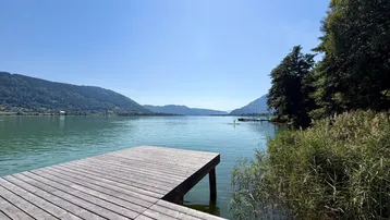 Idyllischer Holzsteg am Seeufer mit weitem Blick auf die umliegende Berglandschaft.