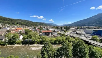Panoramablick über die Stadt mit Fluss, Bergen und umliegender Landschaft unter blauem Himmel.