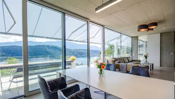 Heller Wohn- und Essbereich mit raumhohen Fenstern, modernem Design und atemberaubendem Seeblick.