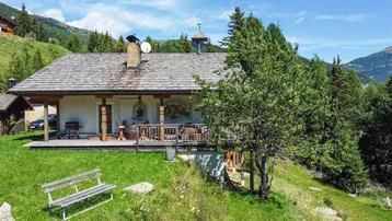 Traditionelles Chalet in alpiner Umgebung mit Holzdach, kleiner Veranda und weitem Bergblick.