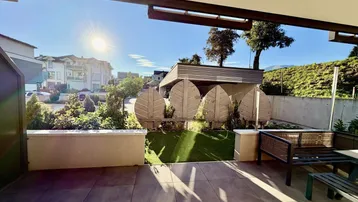 Sonnige Terrasse mit Fliesenboden, Kunstrasen und Blick auf die umliegende Landschaft und Berge.