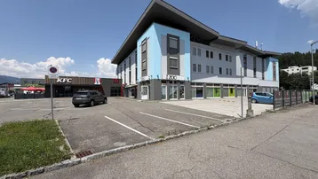 Modernes Gebäude mit blauer Fassade und angrenzendem Parkplatz unter blauem Himmel.