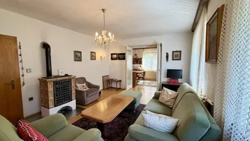 Wohnzimmer mit Kachelofen, bequemen Sofas und traditionellem Teppichboden.