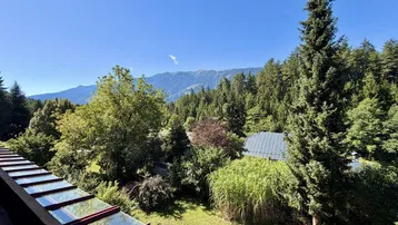 Panoramablick vom Balkon über die grüne Landschaft mit Bäumen und fernen Bergen unter blauem Himmel.