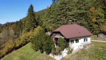 Traditionelles Haus in alpiner Umgebung mit bewaldeten Hügeln und klarem Himmel.