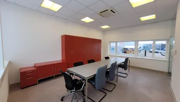Geräumiger Konferenzraum mit großem Tisch, modernen Stühlen und roten Schränken, hell durch große Fenster.