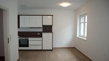 Kompakte Einbauküche mit weißen Schränken und Holzdekor, integriert in einen hellen Raum mit Fenster.