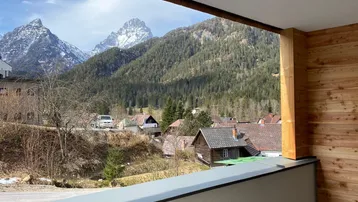 Blick von einem überdachten Balkon auf eine malerische Berglandschaft und ein Dorf.