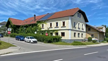Traditionelles Gebäude mit gelber Fassade und roten Dachziegeln an einer Straßenecke.