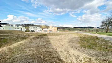 Weitläufiges Grundstück mit Blick auf moderne Häuser und die umliegende grüne Landschaft unter blauem Himmel.