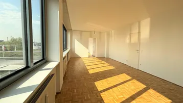 Helles, leeres Zimmer mit großen Fenstern, Parkettboden und viel natürlichem Sonnenlicht.