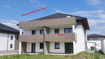 Modernes Mehrfamilienhaus mit Balkonen und gepflegter Grünfläche unter blauem Himmel.