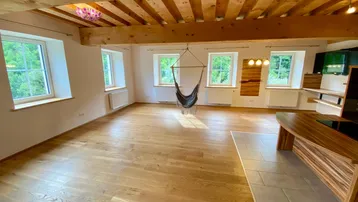 Geräumiger Wohnbereich mit sichtbaren Holzbalken, hellem Parkettboden und großen Fenstern mit Blick ins Grüne.