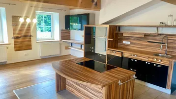 Moderne offene Küche mit Holzfronten, Kochinsel und integrierten Geräten in einem hellen Wohnraum.
