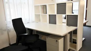 Moderner Arbeitsplatz mit Schreibtisch, Bürostuhl und Regalsystem, gut beleuchtet durch große Fenster.