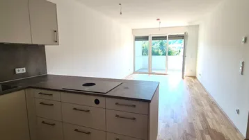 Moderne Einbauküche mit Kochinsel und Holzboden, offen zum hellen Wohnbereich mit Balkonzugang.