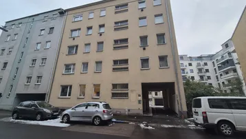 Mehrstöckiges Wohngebäude mit beiger Fassade und geparkten Autos auf der Straße im winterlichen Ambiente.