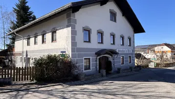Traditionelles Gebäude mit heller Fassade und grauen Akzenten an einer Straßenecke.