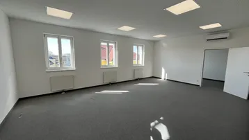 Geräumiger, leerer Büroraum mit grauem Teppichboden, großen Fenstern und Klimaanlage.
