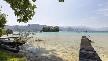 Langer Holzsteg führt ins klare, türkisfarbene Wasser eines Sees mit Bergpanorama im Hintergrund.